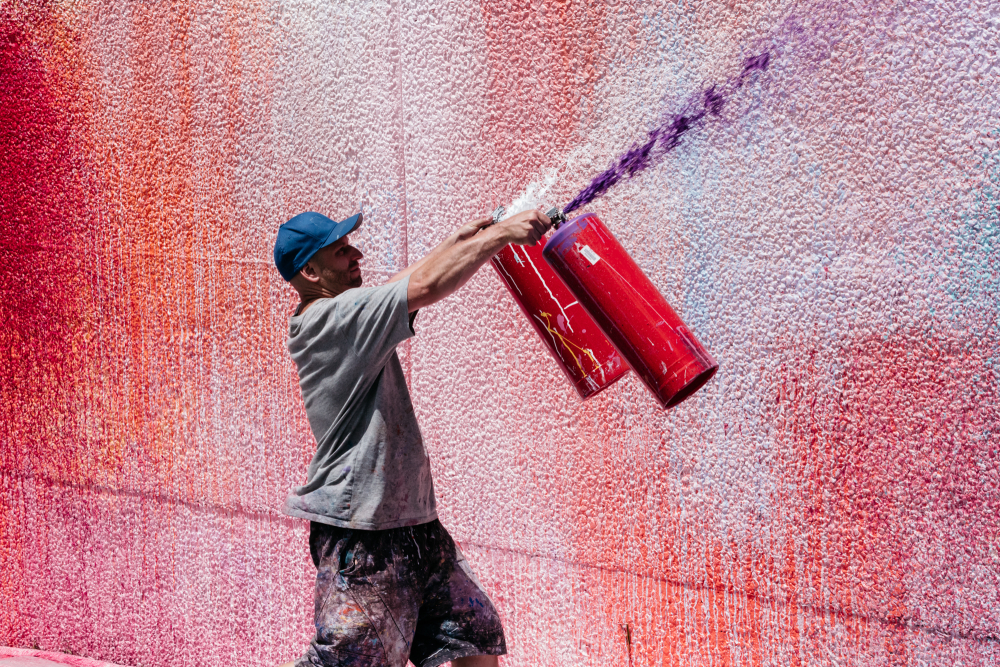 Der australische Künstler Ash Keating beim Bemalen einer Fassade mit farbgefüllten Feuerlöschern, 2018